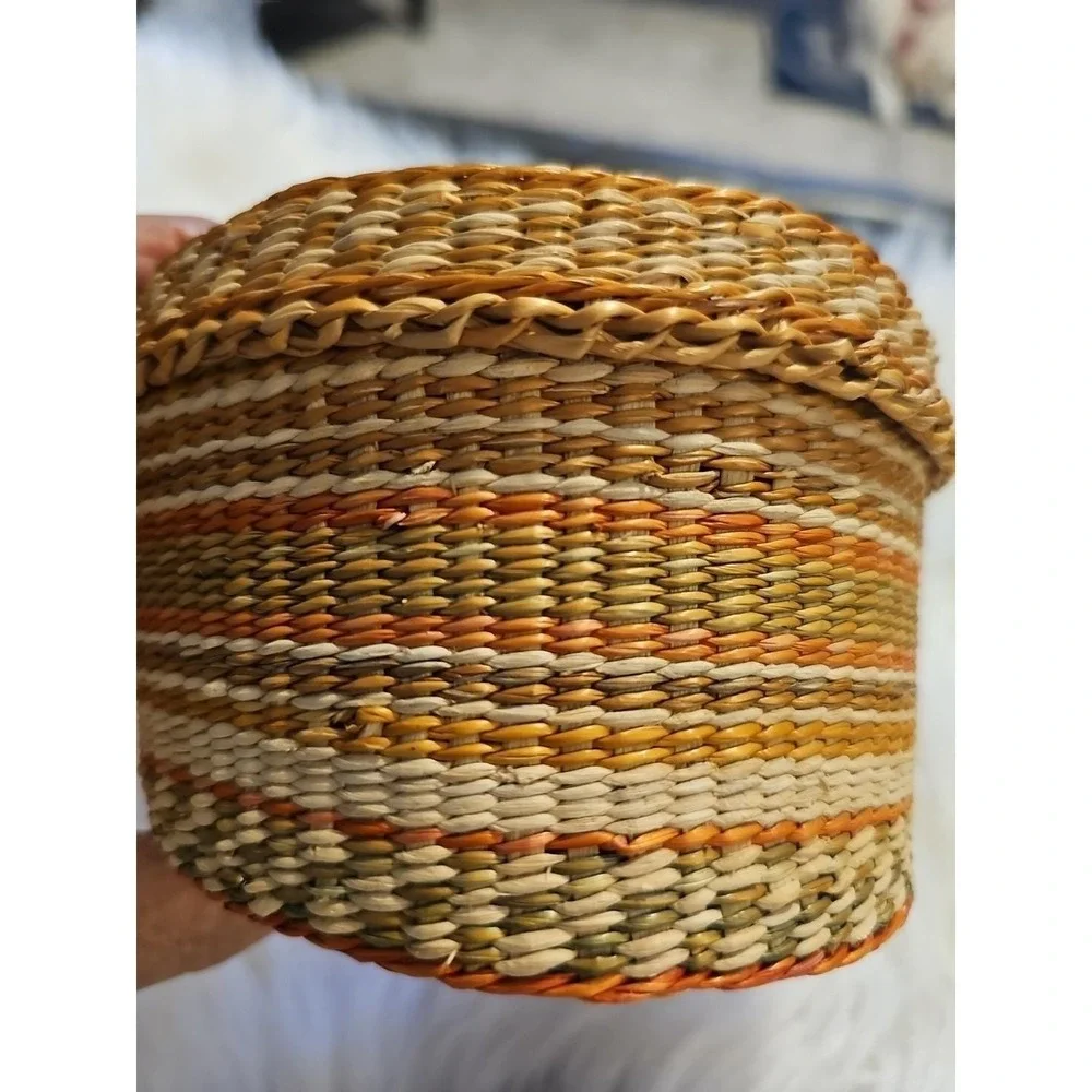 The image displays a‎ small, round, hand-woven basket with a lid, typically made
